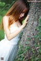 A woman in a white dress leaning against a tree.