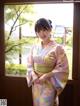 A woman in a pink and green kimono standing by a window.