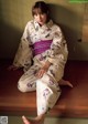 A woman in a kimono sitting on a wooden bench.