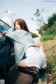 A woman leaning against the side of a car with her back to the camera.