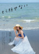 A woman in a blue dress and straw hat sitting on the beach.