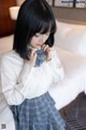 A woman in a white shirt and blue plaid skirt sitting on a bed.