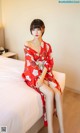 A woman in a red kimono sitting on a bed.