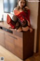 A woman in a red dress and red shoes sitting on a dresser.