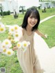 A woman in a beige dress holding a bunch of daisies.