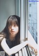 A young woman leaning against a window looking out the window.