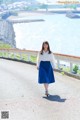 A woman in a white shirt and blue skirt walking down a road.