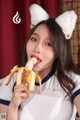 A woman in a white shirt holding a banana in her mouth.