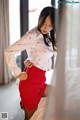 A woman in a white shirt and red skirt posing on a bed.