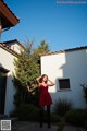 A woman in a red dress standing in front of a house.