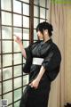 A woman in a black kimono standing by a window.